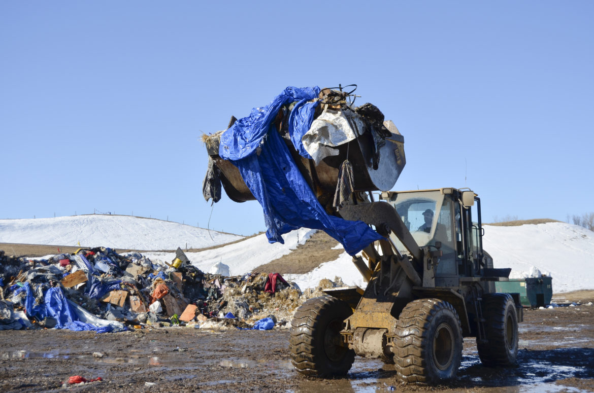 A front end loader picks up debris from camp before loading it on a semi to take it to a disposal site.