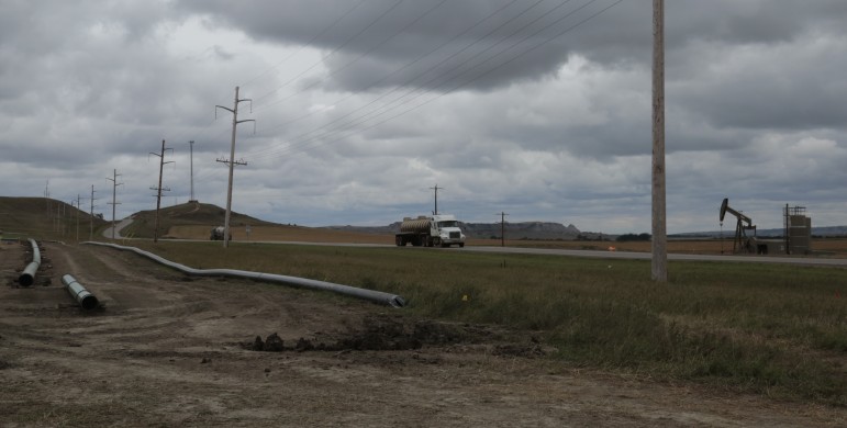 The story of North Dakota's flaring and crude by rail problems in one image: Natural gas flares from an oil well as an oil truck passes a site where a new pipeline is being laid.