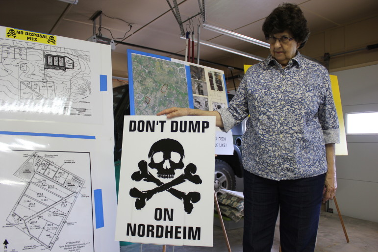 Lyn Janssen in her garage posing with her anti-waste pit posters