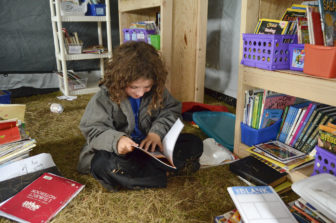Kai Knott, 9, flips through a book in the literacy room of the school at camp. The makeshift school is contained in several large tents for now, but those in charge of the facility plan to build a more permanent structure to endure the winter.